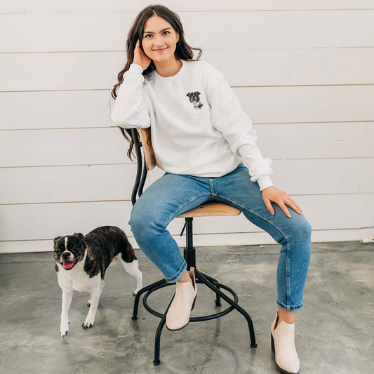 Woman sitting on a chair with a dog standing next to her against a white wall.