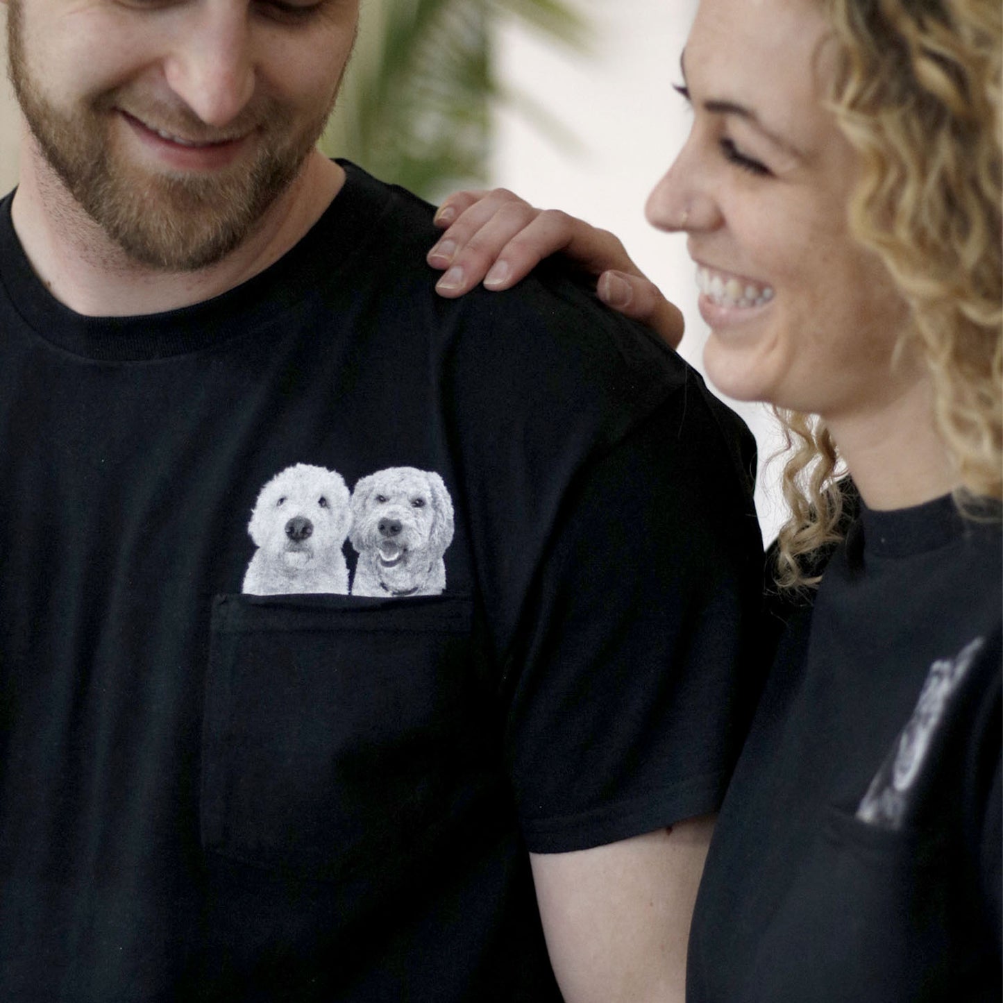 Two people wearing black t-shirts with dog illustrations, one of which is being petted.