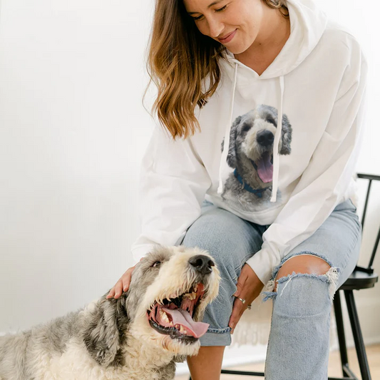 Woman wearing a hoodie with a dog's face printed on it, sitting next to a large dog.