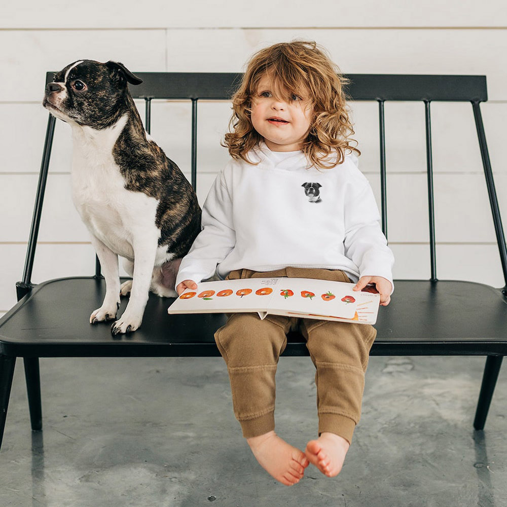 Child sitting on a bench with a dog, holding a book with illustrations of animals.