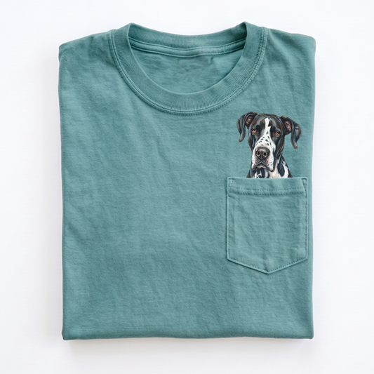 A folded teal crewneck t-shirt with a chest pocket featuring a printed illustration of a black and white Great Dane dog's face peeking out, set against a plain white background.