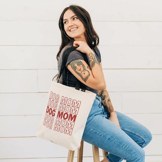 Woman holding a tote bag with 'DOG MOM' text against a white wooden background